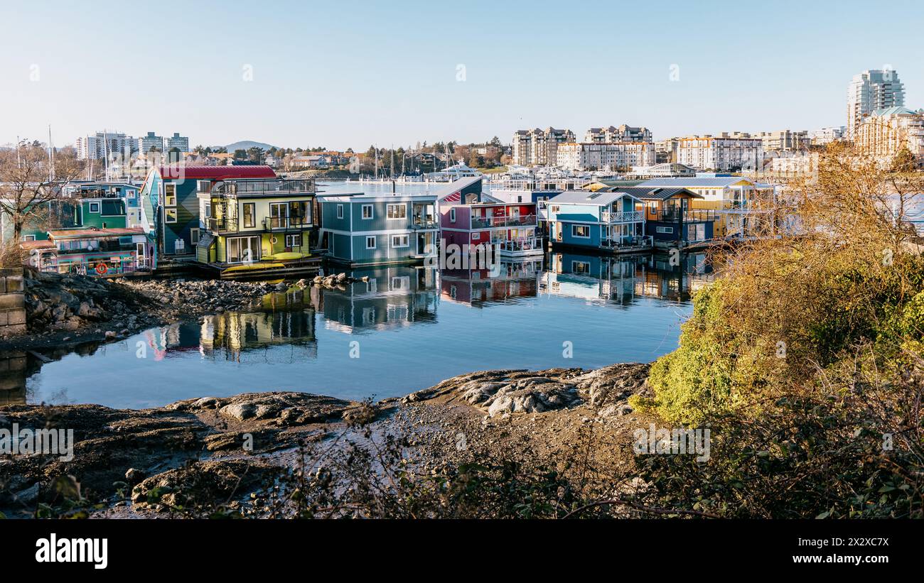 Victoria, Canada - 17 marzo 2024: Una fila di case galleggianti colorate al Fisherman's Wharf, che catturano la splendida luce del sole riflessa dal mare. Foto Stock