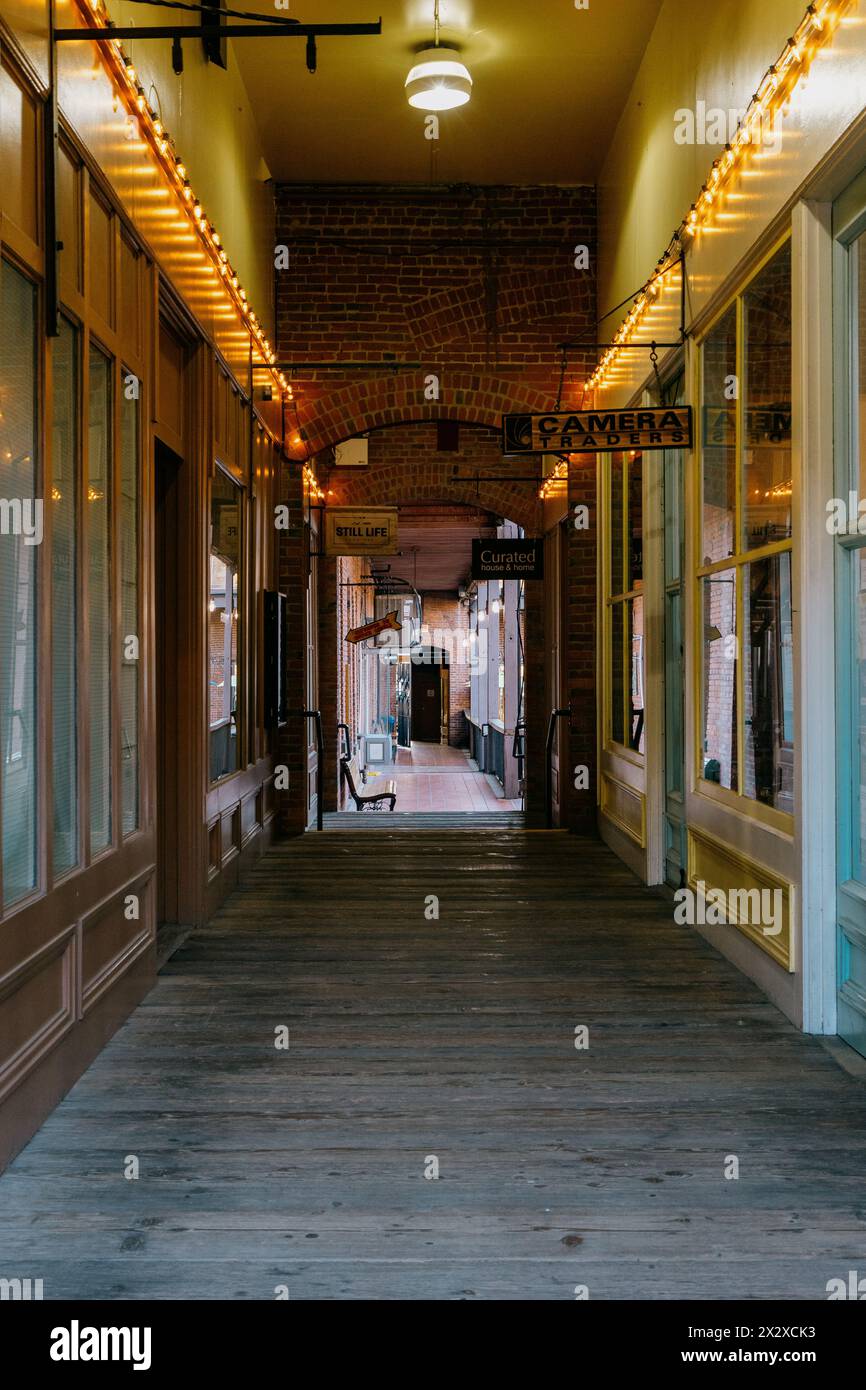 Victoria, Canada - 18 marzo 2024: Una galleria con pavimento in legno e negozi con cartelli che si aprono su un balcone illuminato dal sole sulla piazza del mercato Foto Stock