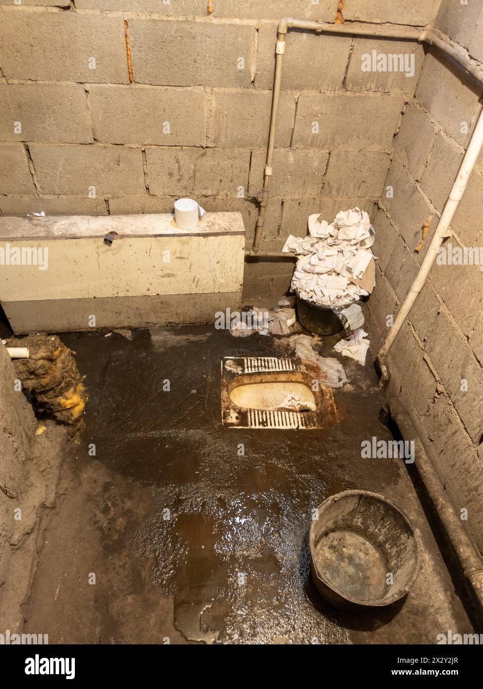 Il bagno era sporco, con un mucchio di carta igienica usata e un secchio, pavimento in cemento non rivestito e pareti in mattoni di cenere. Foto Stock