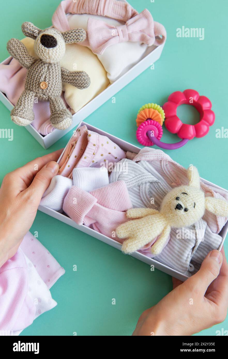 Le mani delle donne raccolgono i vestiti dei bambini in scatole. Il concetto di preparazione alla nascita di un figlio o di donazione. Foto Stock