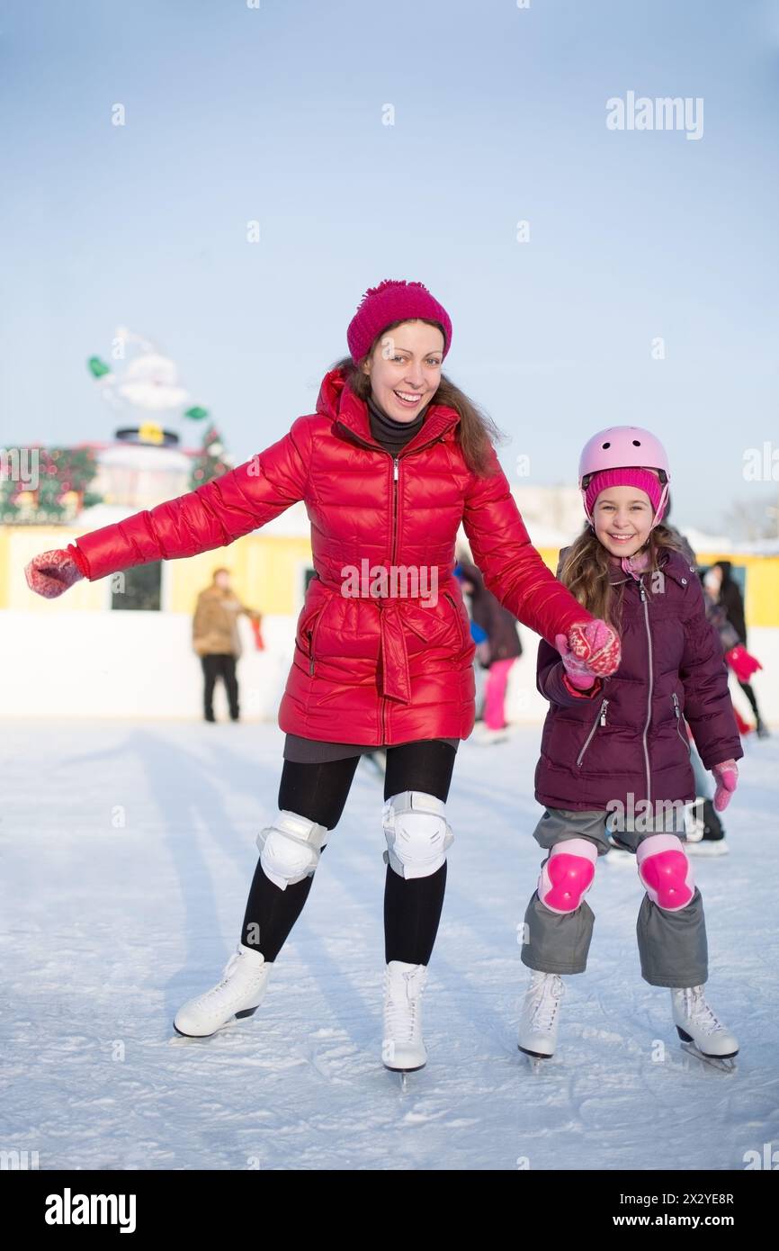 Mamma e figlia felici pattinano sulla pista di pattinaggio all'aperto in inverno Foto Stock