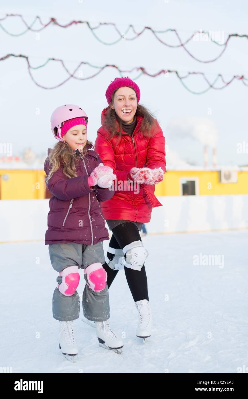 Mamma e figlia felici modellano le palle di neve sulla pista di pattinaggio all'aperto in inverno Foto Stock