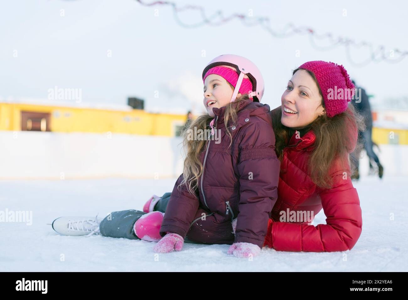 Madre e figlia felici sedute sulla pista di pattinaggio all'aperto in inverno Foto Stock