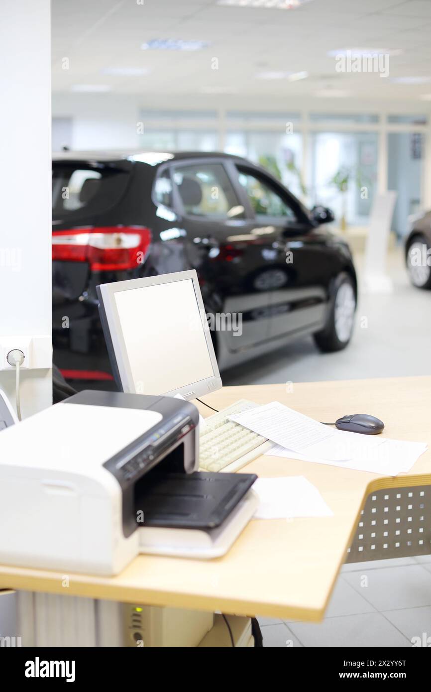 Computer, stampante e documenti su una scrivania in legno e nuovi stand per auto nell'ufficio del negozio di automobili. Profondità di campo ridotta. Messa a fuoco sul display. Foto Stock