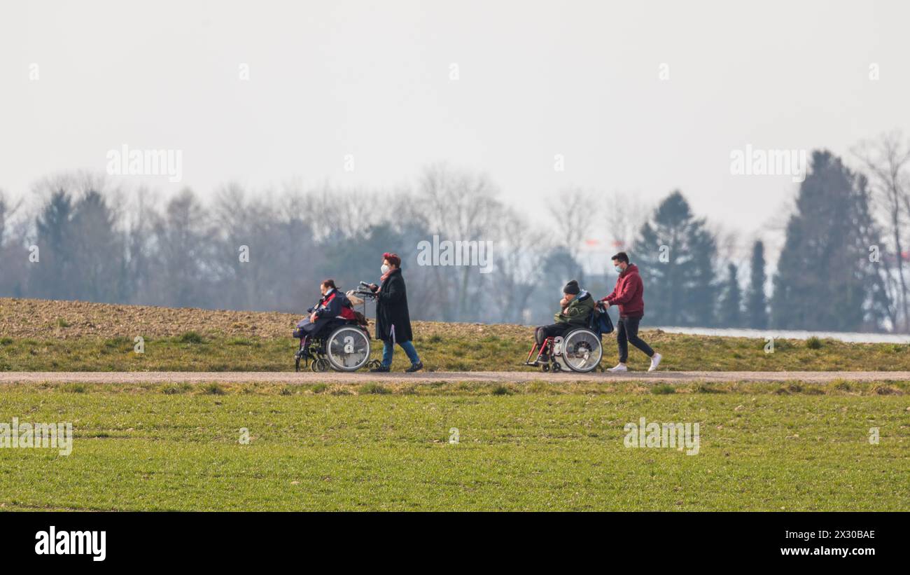 Zürich, Schweiz - 12. März 2022: Betreuer sind mit Menschen mit einer körperlichen Beeinträchtigung mit dem Rollstuhl unterwegs. Die ersten wärmenden Foto Stock