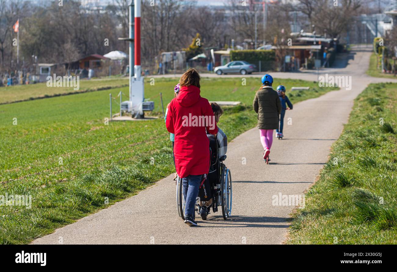Eine Frau schriebt einen Menschen in einem Rollstuhl. (Kloten, Schweiz, 19.03.2022) Foto Stock