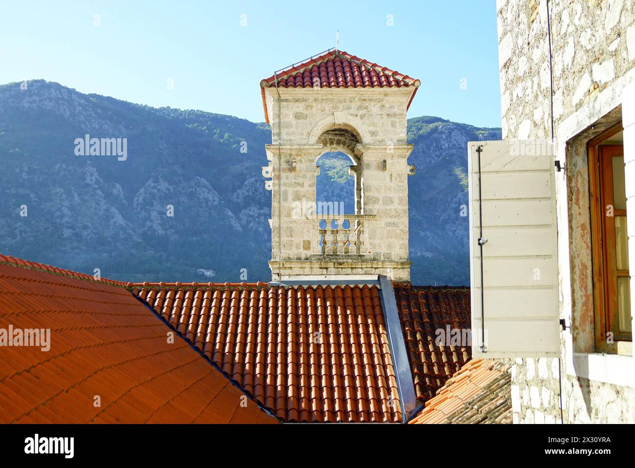 Tetti di tegole rosse e campanile quadrato della Chiesa di San Francesco nella città vecchia di Cattaro sullo sfondo della montagna. Foto Stock
