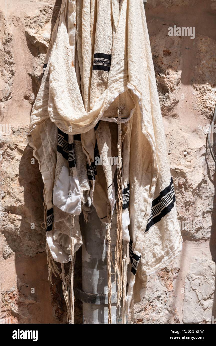 Uno scialle di preghiera ebreo sporco, lacerato e lacerato o tallit appeso a una pipa lungo il muro di un vecchio edificio in pietra nel quartiere di Mea She'arim Foto Stock