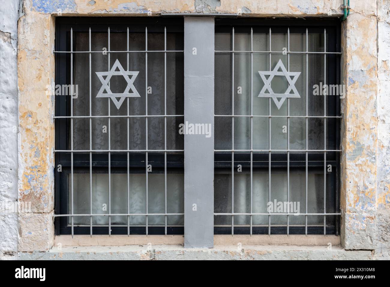Un paio di finestre in un vecchio palazzo di Gerusalemme nel quartiere di Mea She'arim con una griglia di metallo e stelle ebraiche di David. Foto Stock