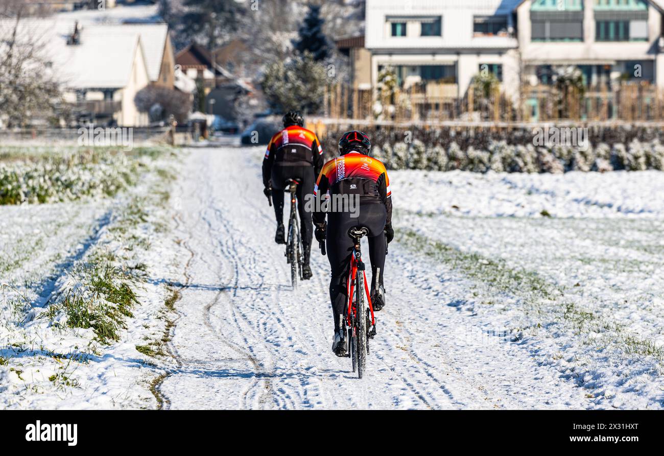 Auf schneebedeckter Strasse fahren zwei Personen bei winterlichen Strassenverhältnisse mit dem Rennrad. (Rafz, Schweiz, 11.12.2022) Foto Stock