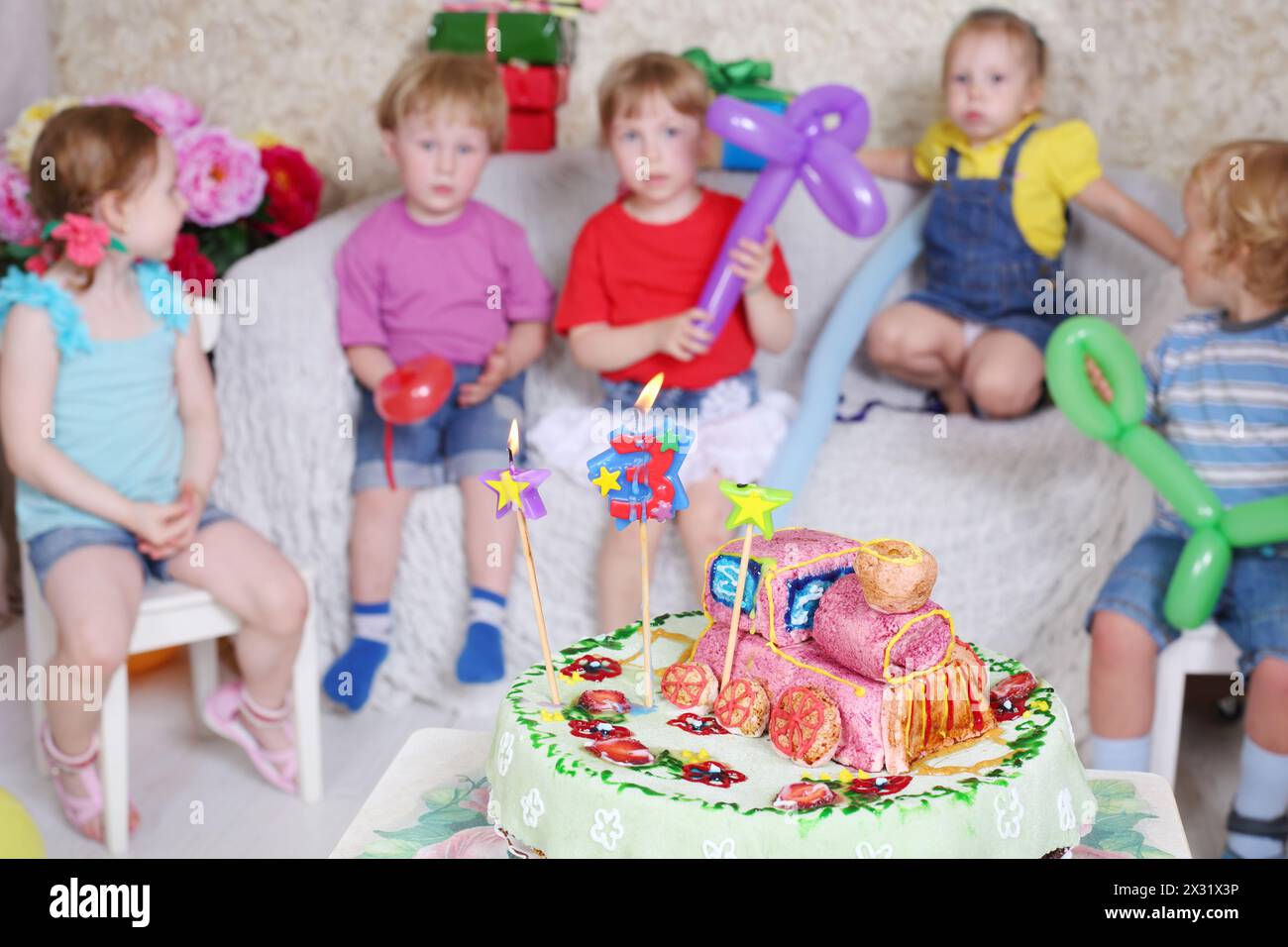La torta di compleanno è sul tavolo e cinque bambini si aspettano delle delizie alla festa dei bambini. Concentrati sulla torta. Foto Stock