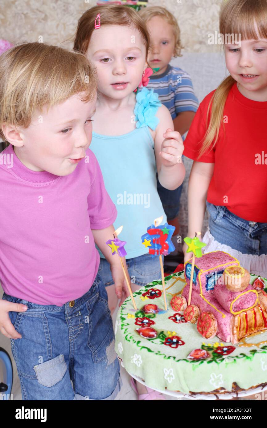 Il ragazzo di compleanno fa saltare le candele sulla torta e tre suoi amici lo guardano alla festa dei bambini. Foto Stock
