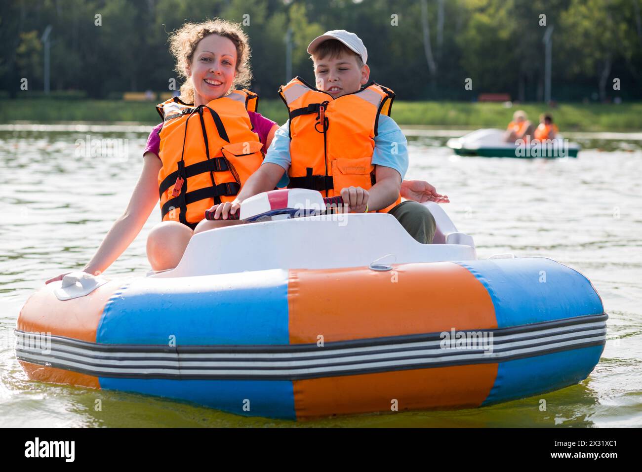Figlio e madre nei giubbotti di salvataggio che galleggiano lungo il fiume in una barca di gomma con ruota elettrica Foto Stock