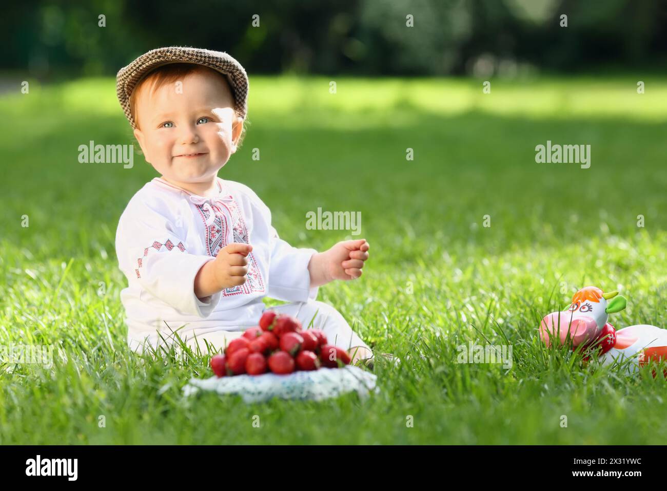 Bambino in costume nazionale russo seduto sull'erba vicino al piatto con fragole Foto Stock