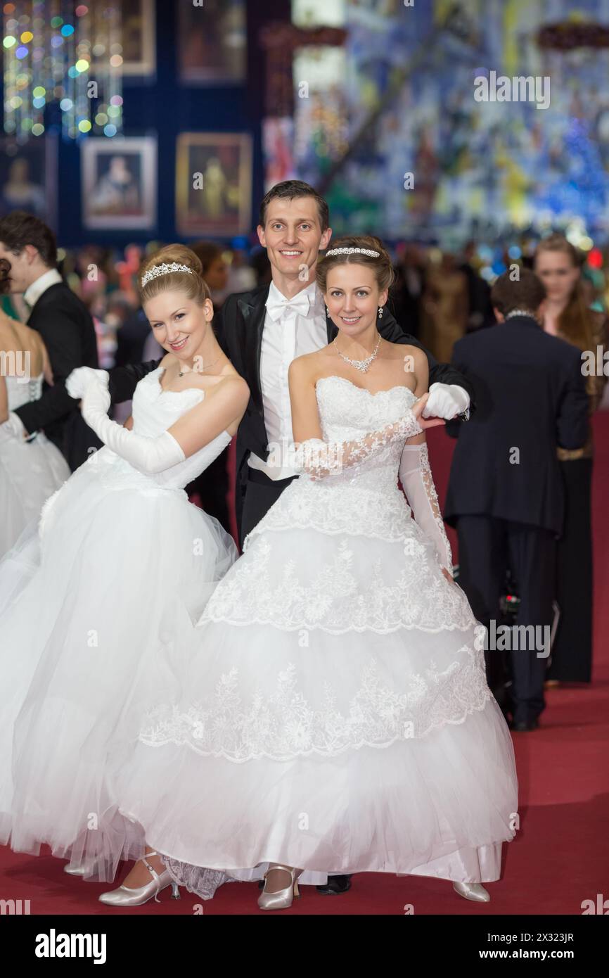 Due ragazze sorridenti in elegante abito bianco e un uomo in smoking al ballo viennese Foto Stock