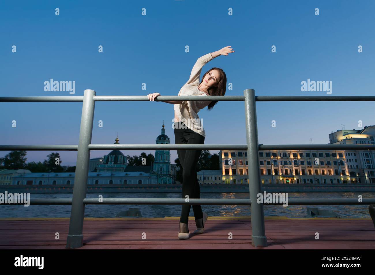 Una giovane donna è in piedi in una posizione di balletto usando come sbarra la ringhiera sul lungomare Foto Stock