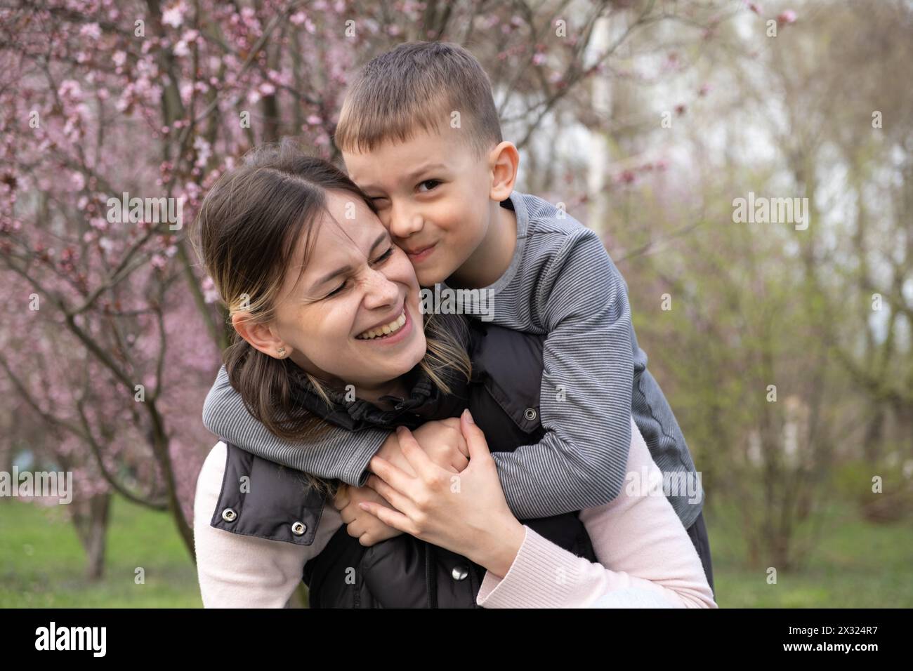 Mamma e figlio felici che si abbracciano tra i fiori di ciliegio in primavera. Foto Stock