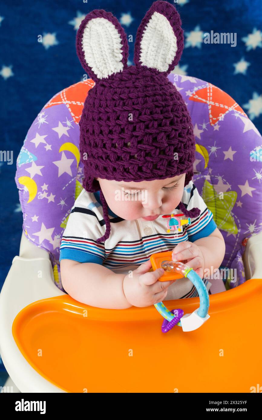 Un bambino con un cappello a maglia con orecchie di coniglio gioca con un giocattolo Foto Stock