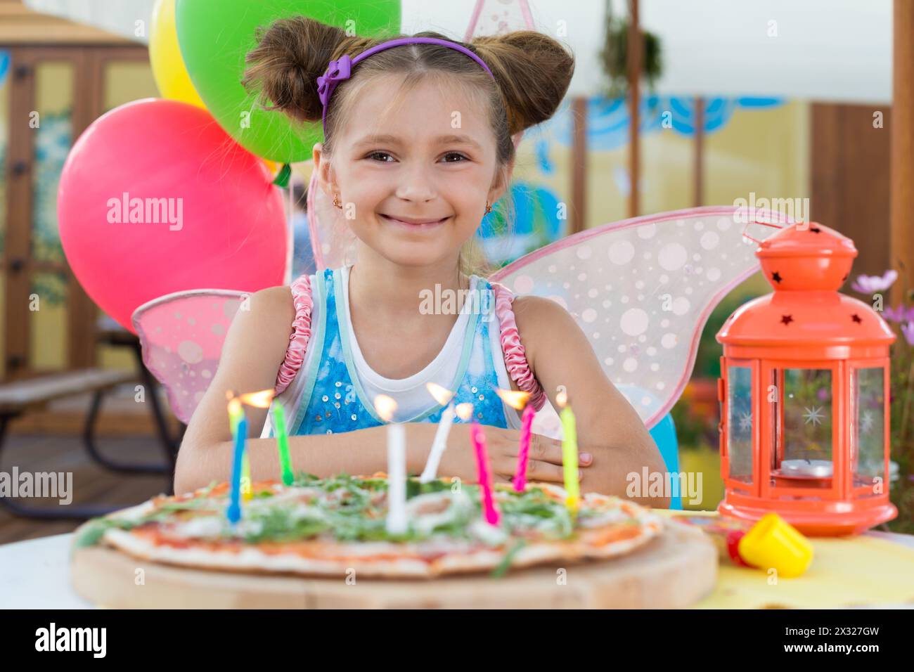 Ragazza sorridente in costume da fata con candele bruciate nella pizza Foto Stock