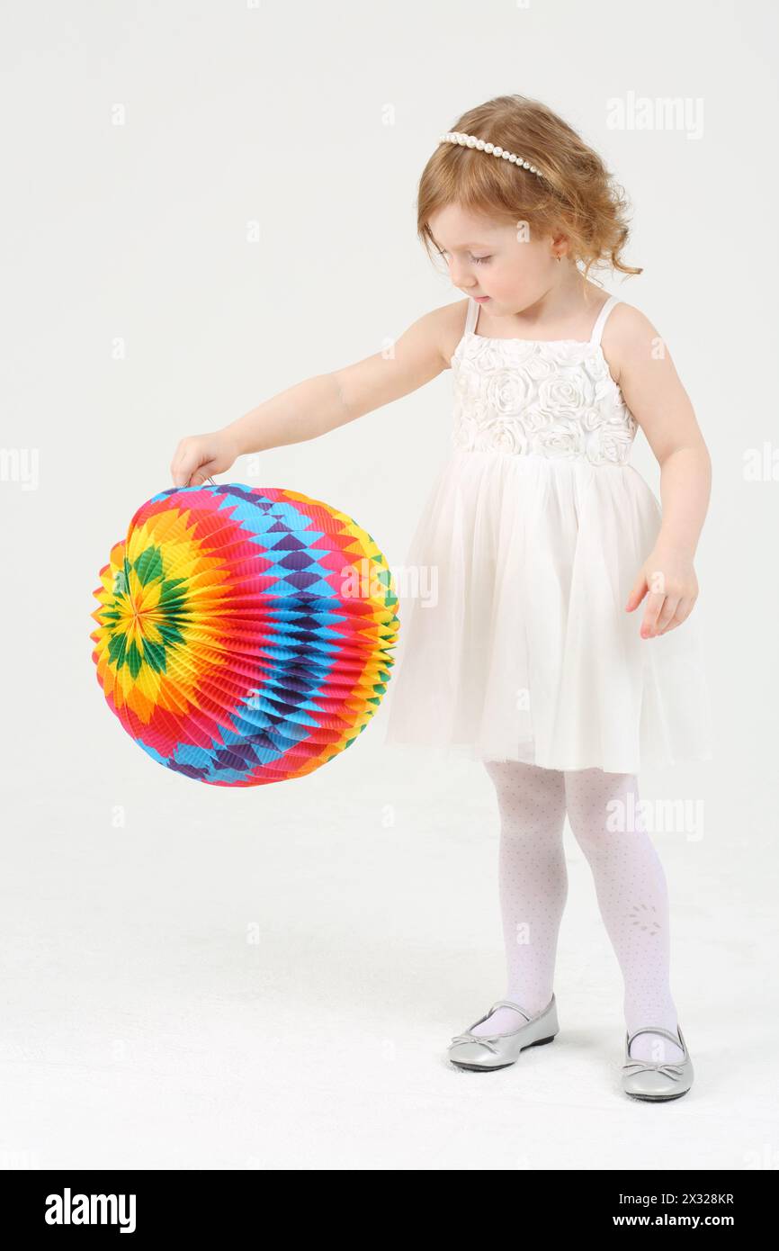 La bambina in abito bianco gioca con la palla multicolore su sfondo bianco. Foto Stock