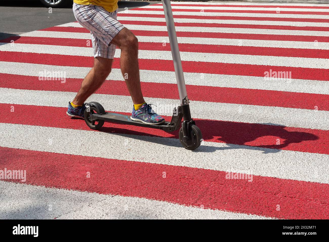 Dettaglio di un uomo che guida un kick scooter non elettrico in un crosswalk. Trasporto Foto Stock