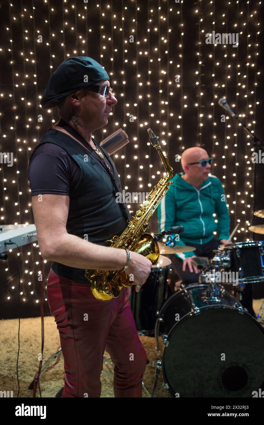 Sassofonista in cappello e occhiali da sole che suona il sassofono con il batterista in un club con ghirlande Foto Stock