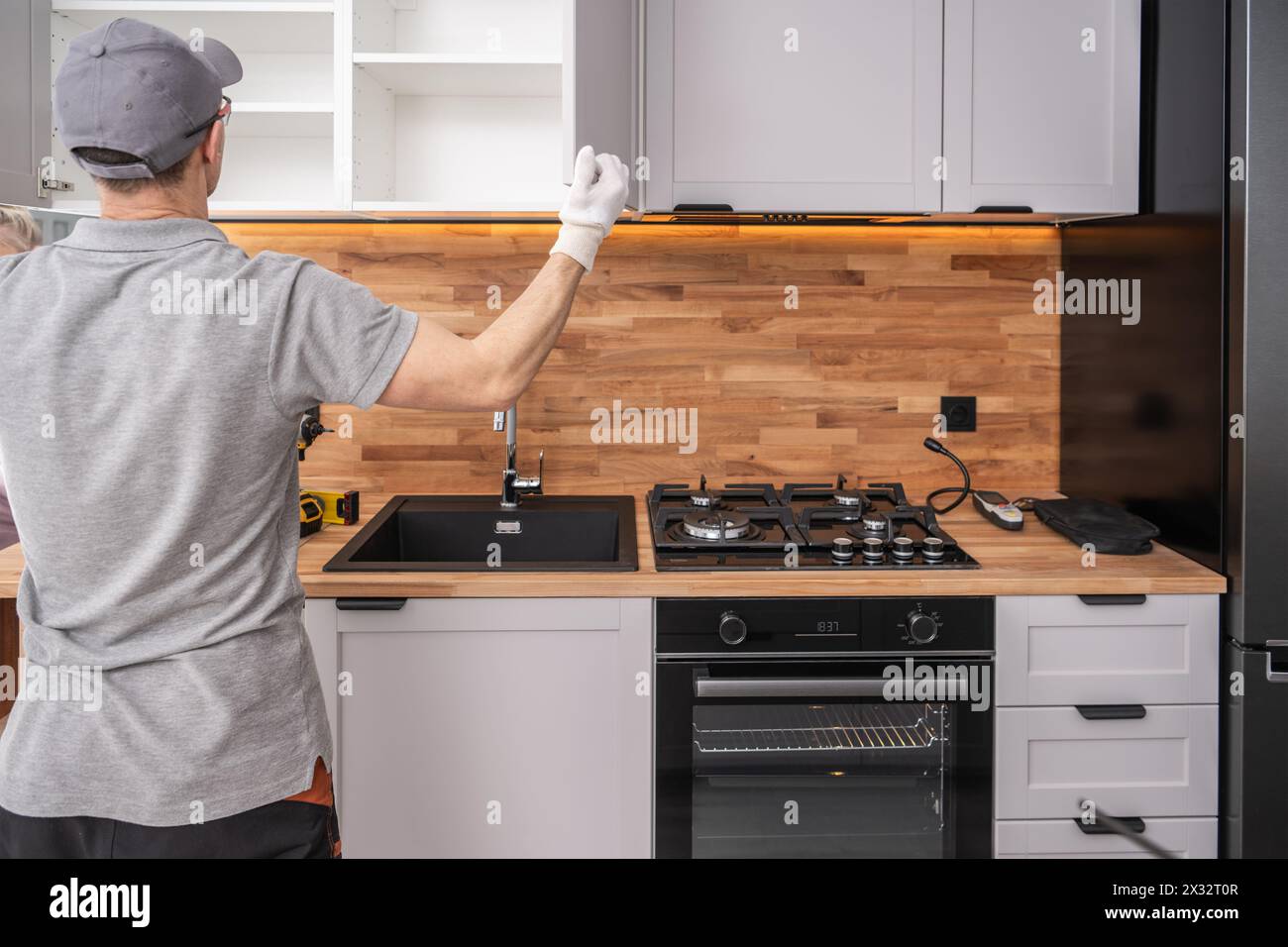 Armadietti caucasici nella sua installazione di armadi da cucina con finitura anni '40. Cucina moderna bianca ed elegante. Foto Stock