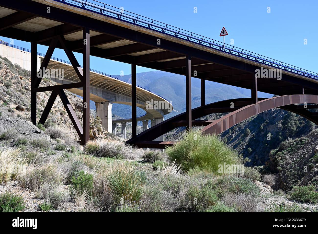Vecchio ponte stradale in acciaio accanto a un più moderno ponte di cemento sul burrone nel villaggio di Ízbor, Spagna, in un habitat roccioso secco Foto Stock