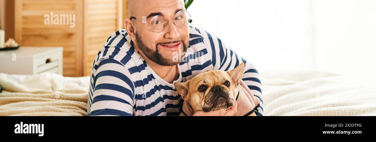L'uomo elegante con gli occhiali coccola un piccolo bulldog francese a casa. Foto Stock
