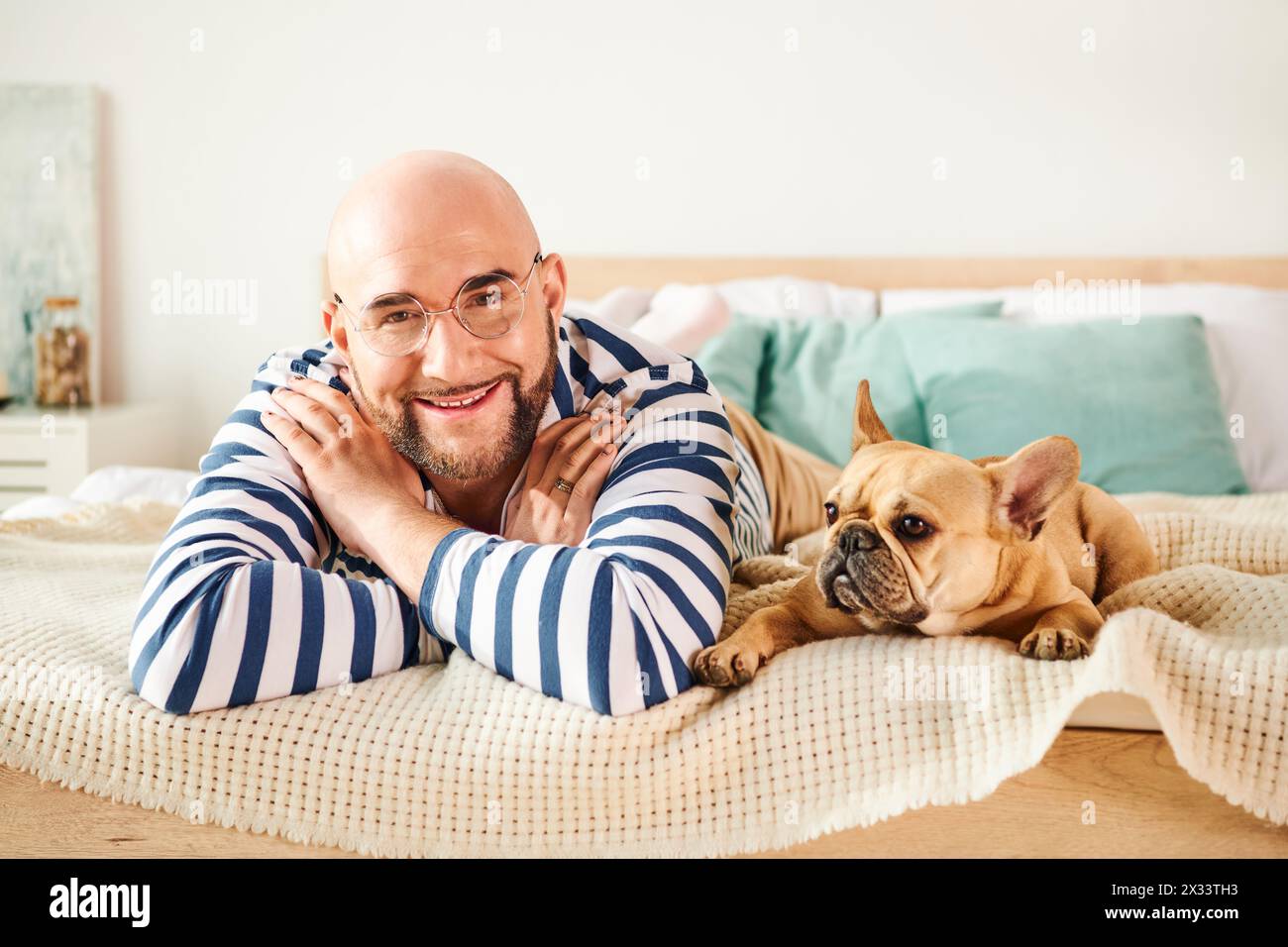 Bell'uomo con occhiali che si rilassa sul letto accanto al suo fedele Bulldog francese. Foto Stock