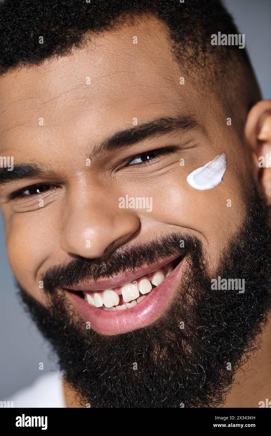 Uomo afroamericano alla moda con una barba che mostra crema bianca sul viso. Foto Stock
