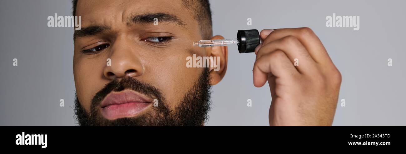 Uomo afroamericano elegante con barba che regge una bottiglia di siero. Foto Stock