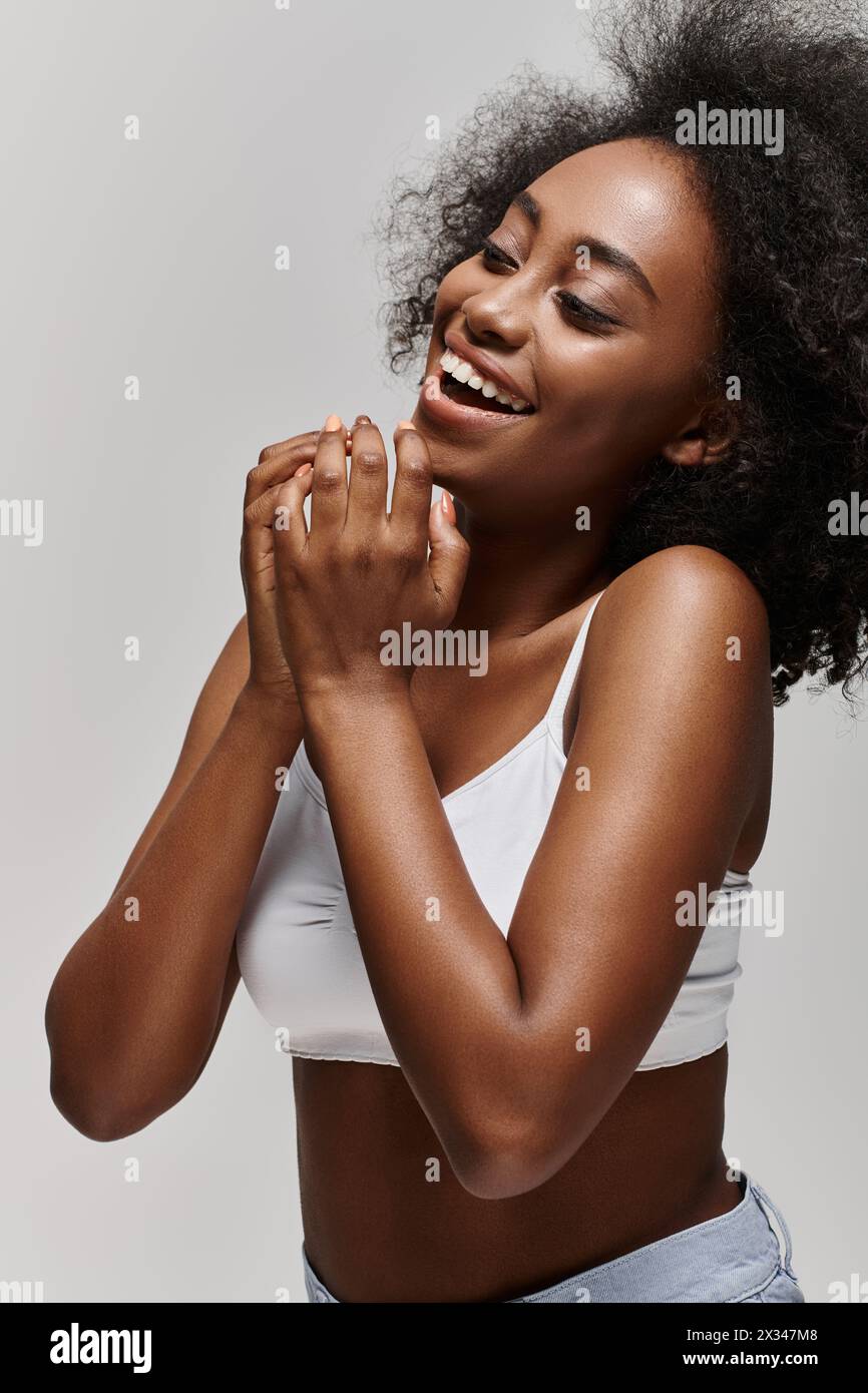 Una bella giovane donna afroamericana con i capelli ricci che indossa un top bianco, che sorride brillantemente e batte le mani. Foto Stock