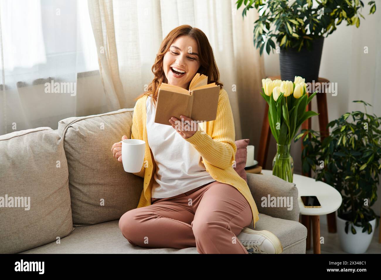 Donna di mezza età infilata in un libro mentre era seduta su un comodo divano. Foto Stock