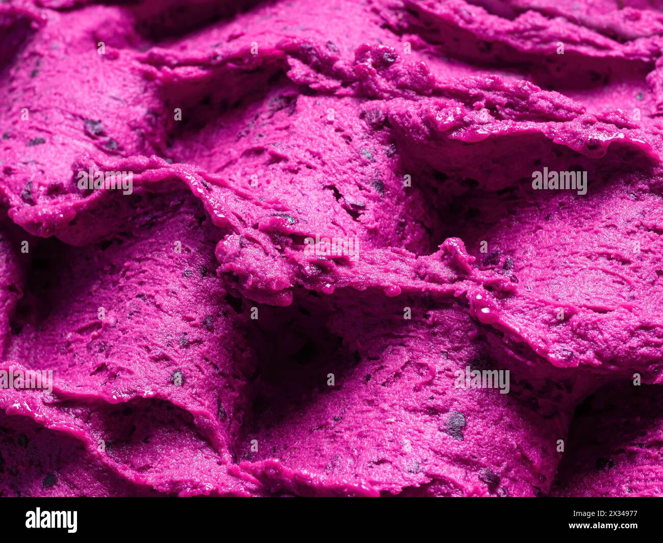 Gelato al lampone congelato - dettaglio completo del sorbetto. Primo piano di una superficie rosa di gelato riempita con pezzi di frutta mista. Foto Stock