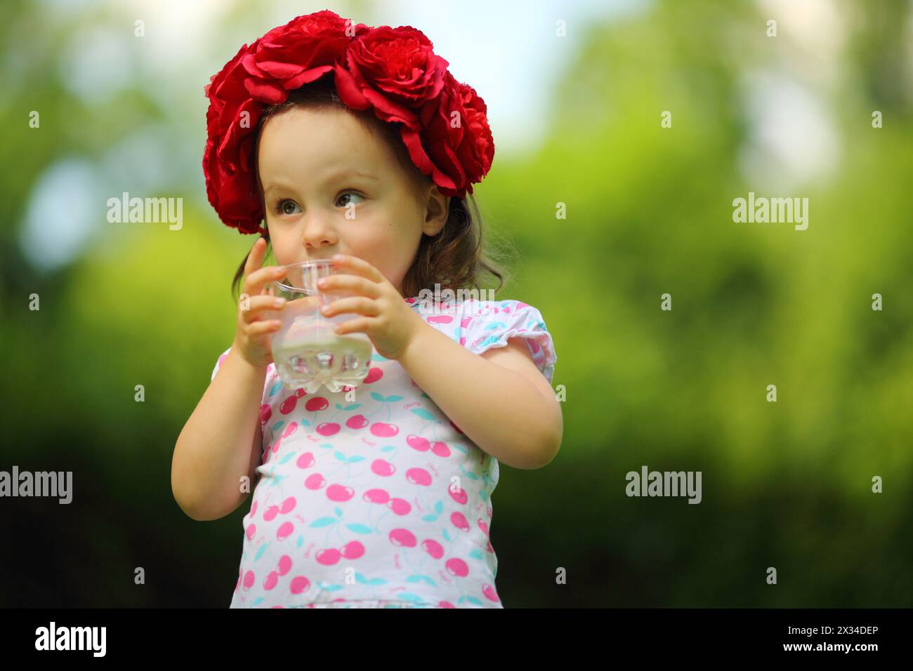 La bambina carina nella corona di fiori beve latte nel parco estivo, poco profonda dof Foto Stock