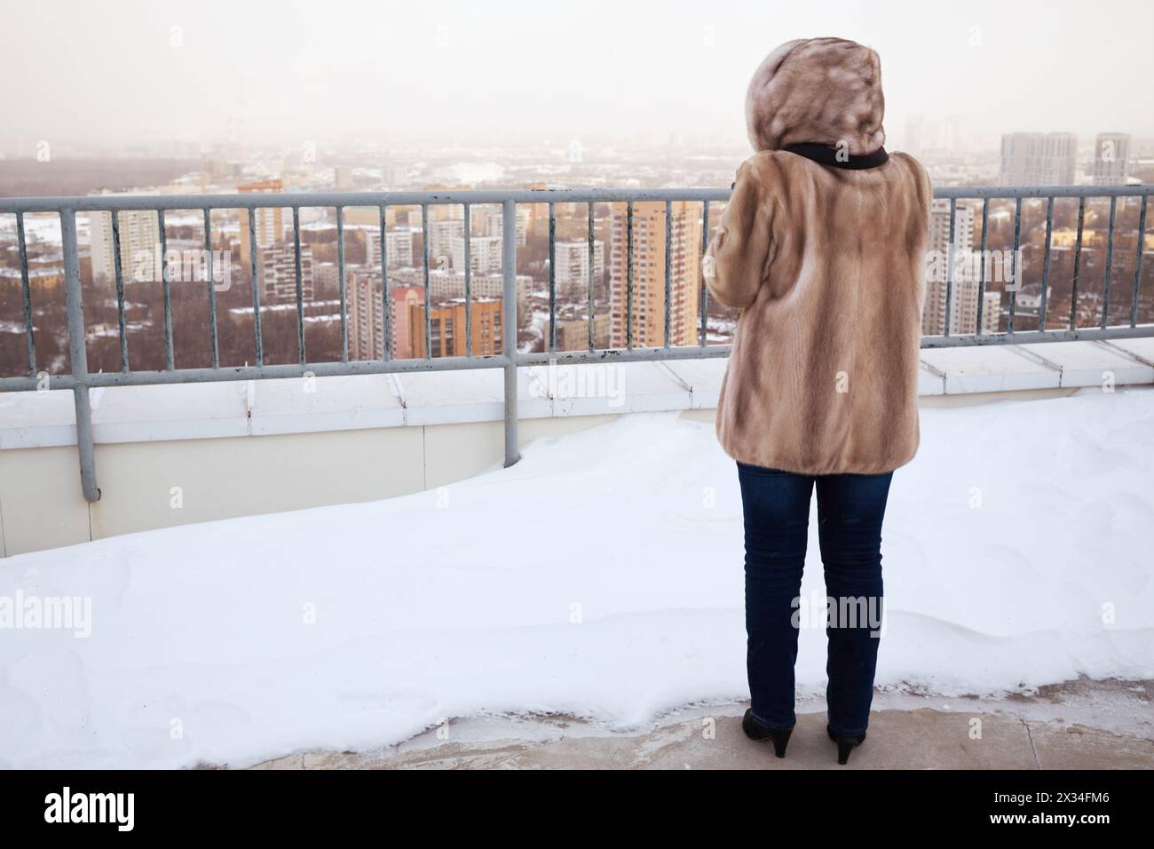 Donna con giacca in pelliccia sul tetto dell'edificio con sponda di neve in inverno, vista posteriore. Foto Stock