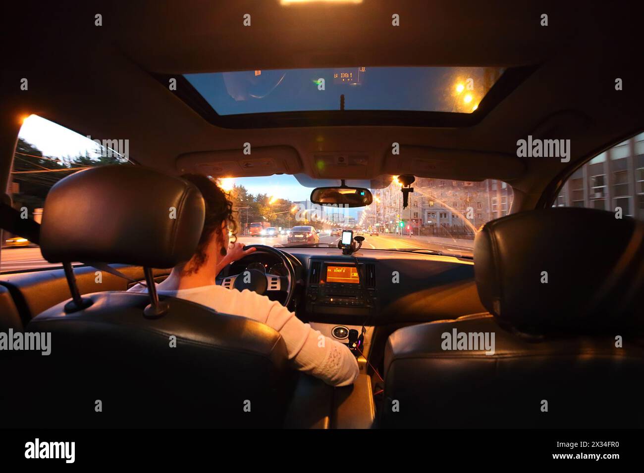 Guidare un'auto di notte - giovane donna che guida la sua auto. Vista dai sedili posteriori dell'auto, focalizzata sulla strada. Foto Stock