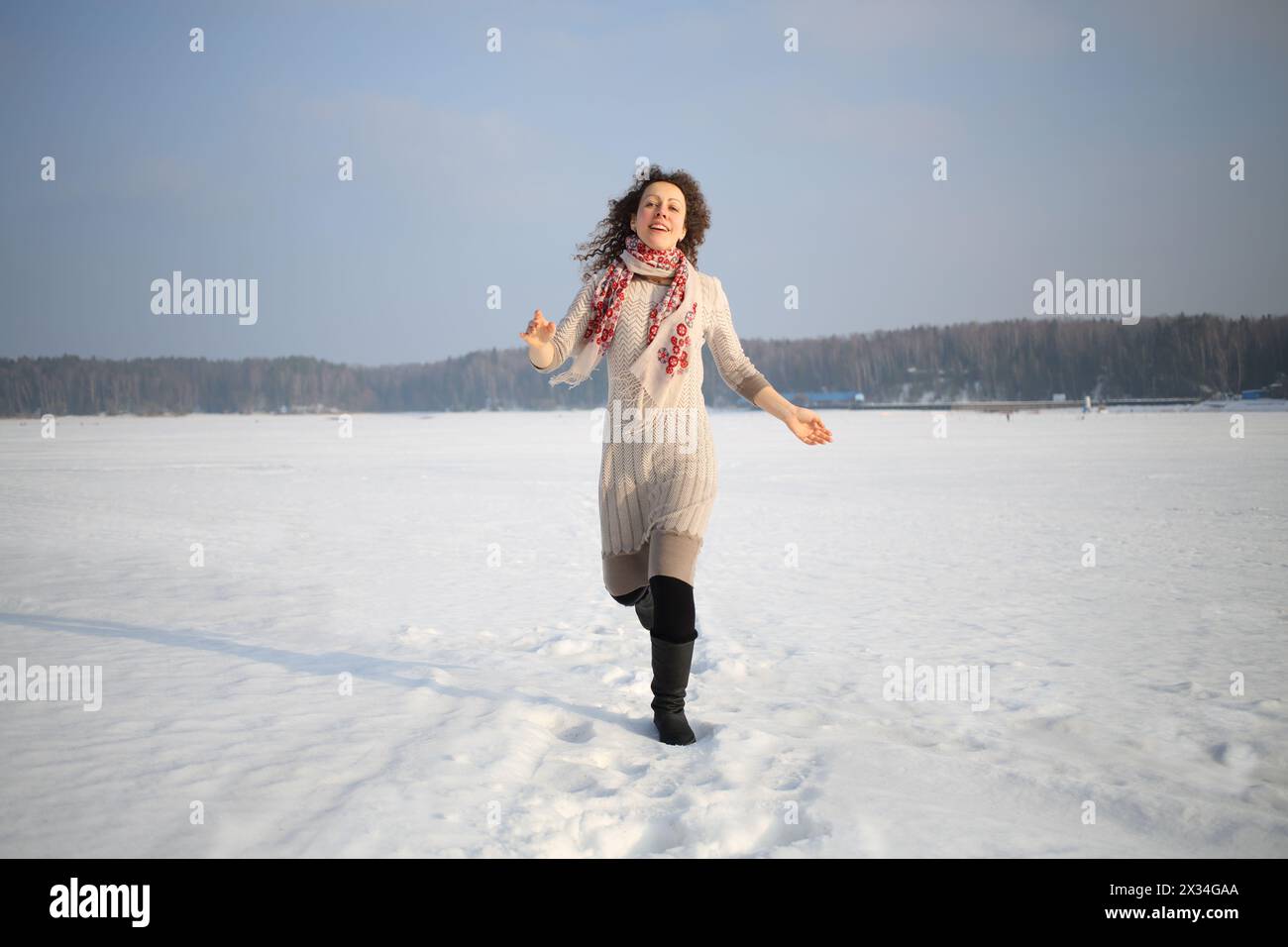 Bella donna con capelli ricci in un abito beige che corre sulla neve Foto Stock