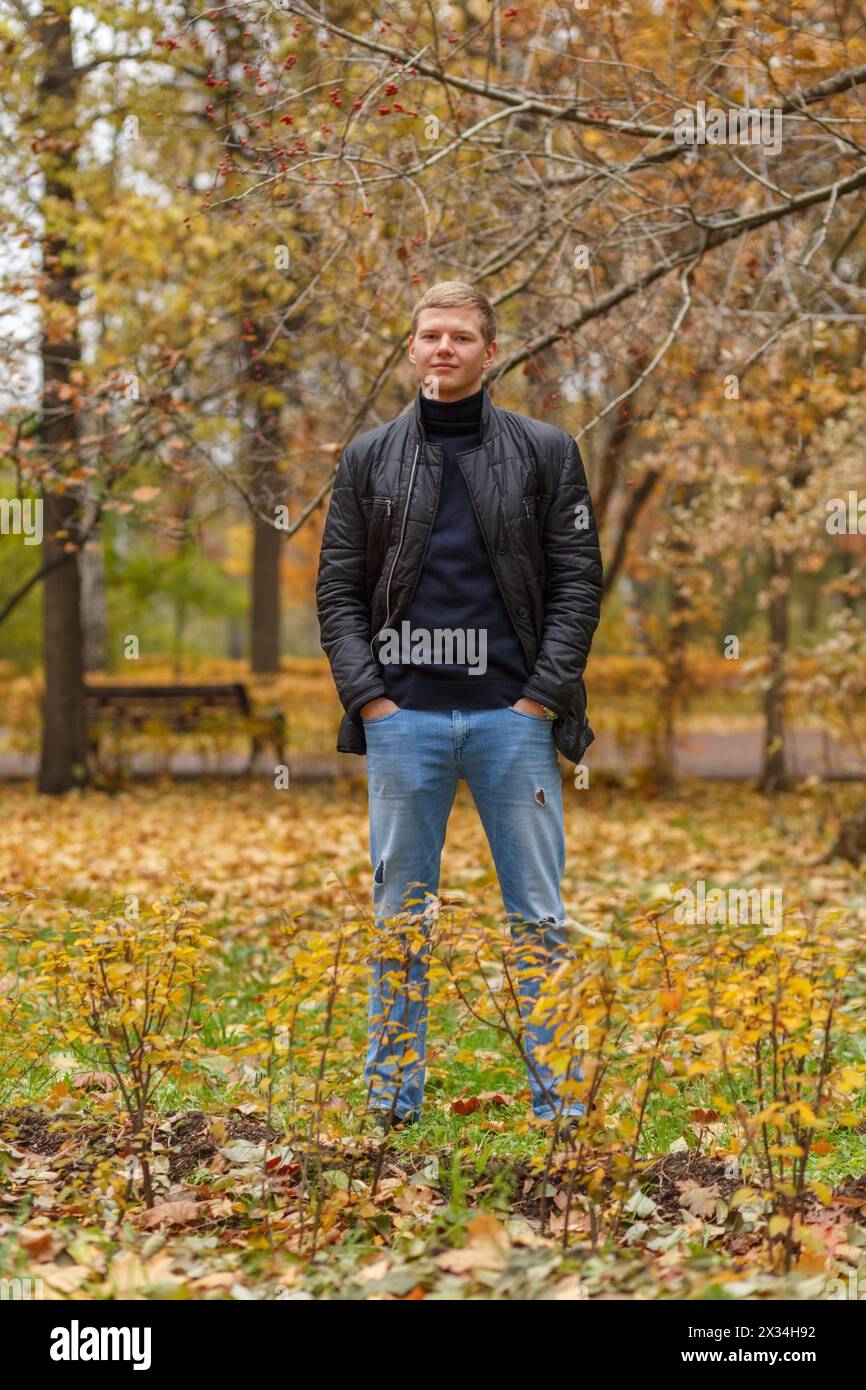 Ritratto in piena crescita giovane uomo in giacca nera nel parco autunnale Foto Stock