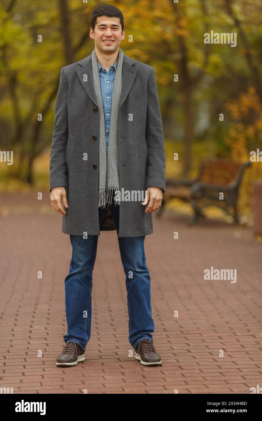 Ritratto in piena crescita giovane uomo in cappotto grigio nel parco autunnale Foto Stock