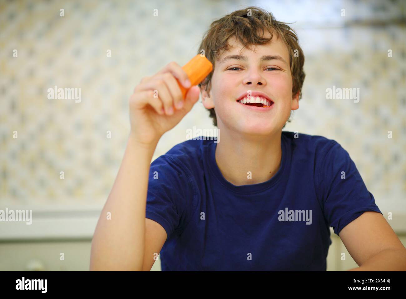 Ragazzo felice in camicia blu scuro che mangia carote pulite, vista ravvicinata Foto Stock