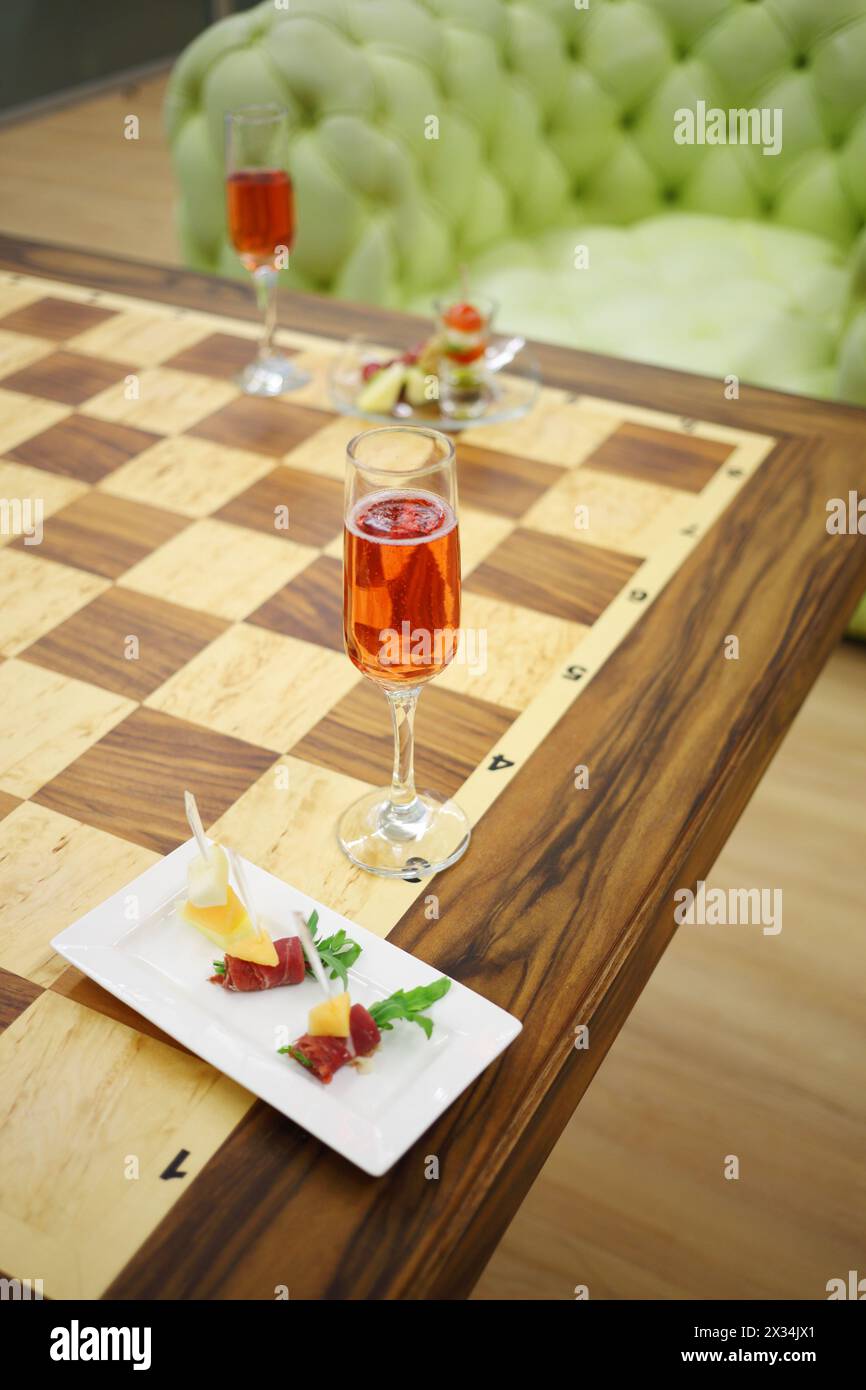 Stuzzichini, piatti freddi e bicchiere con spumante rosa al tavolo Foto Stock