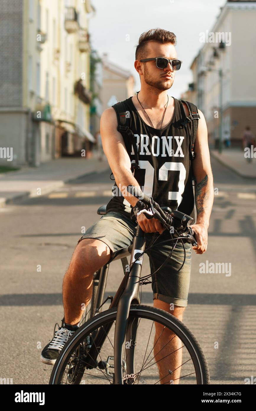 Giovane Hipster con bicicletta seduta su Una bicicletta in città. T-shirt nera con Stampa 23 Foto Stock