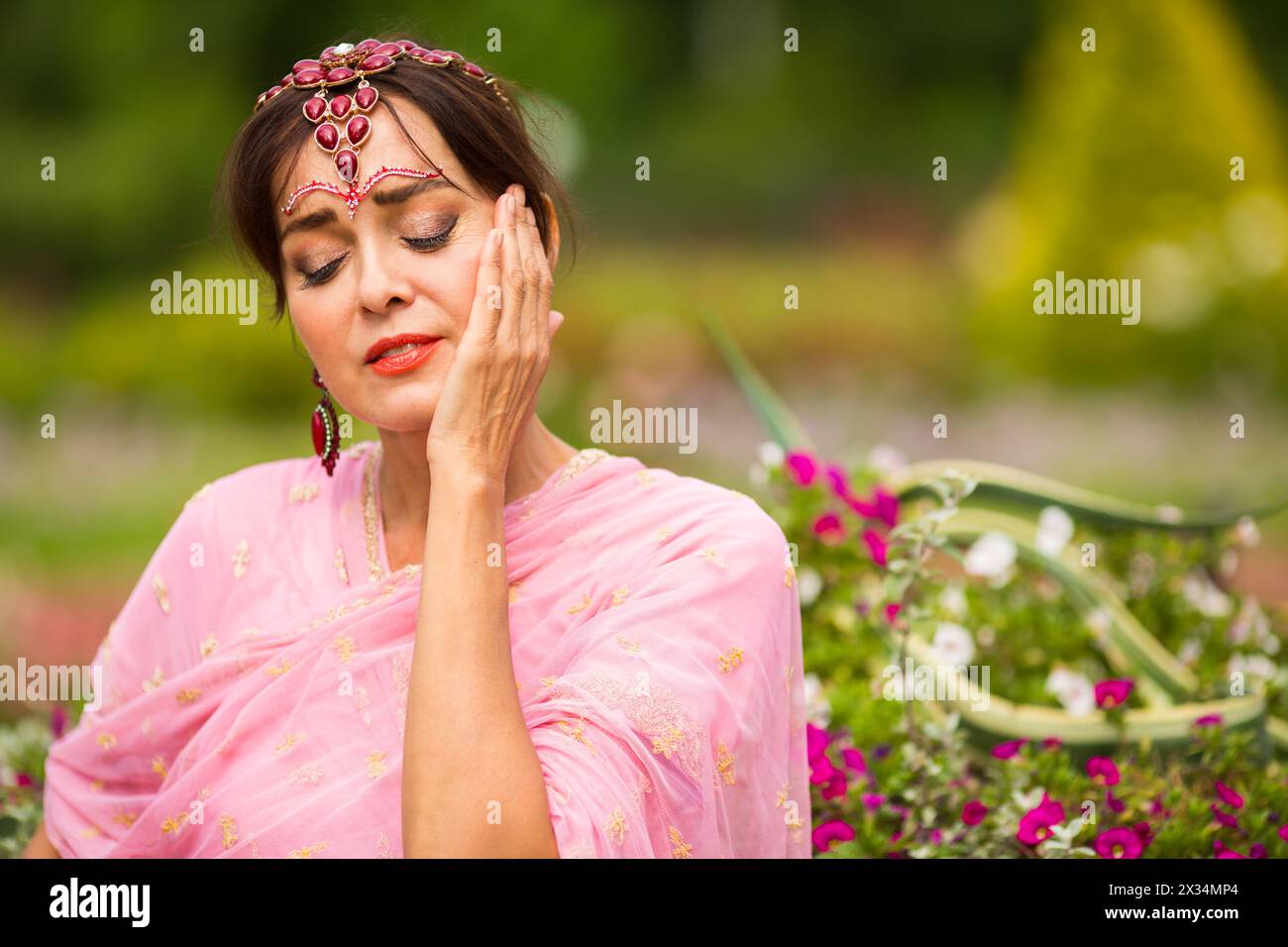 Donna di mezza età in sari rosa e adornamento indiano che si gode nel parco estivo Foto Stock
