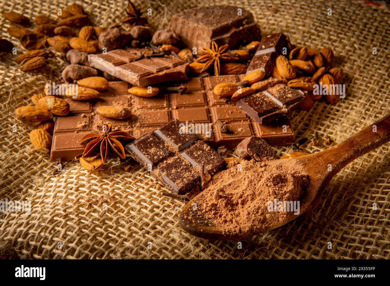 Natura morta di diversi tipi di cioccolato con mandorle e spezie come anice stellato e chiodi di garofano su un sacco Foto Stock