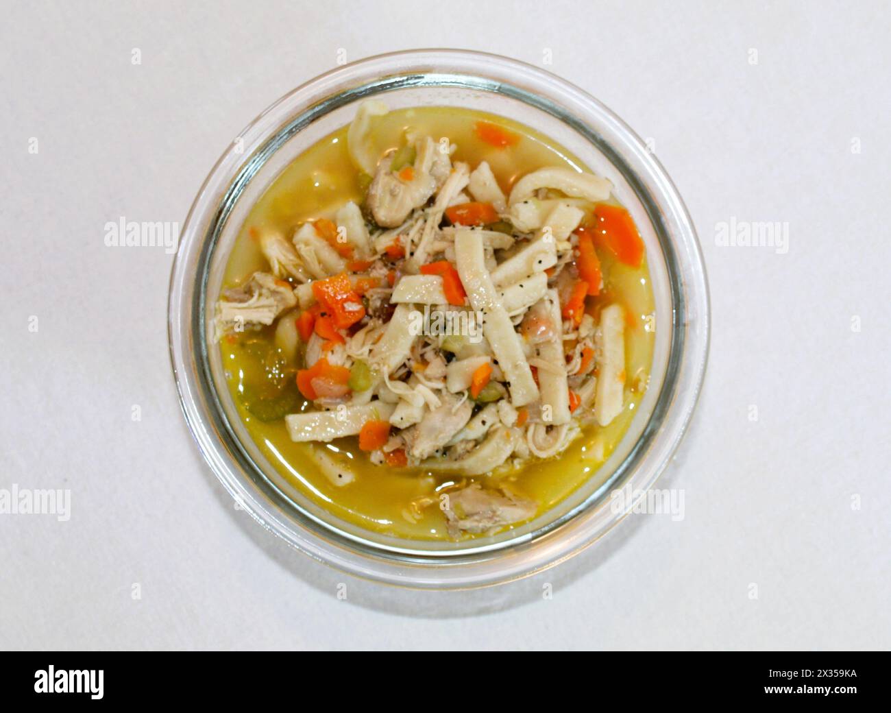 Zuppa di noodle di pollo fatta in casa in un recipiente di vetro con fondo semplice Foto Stock