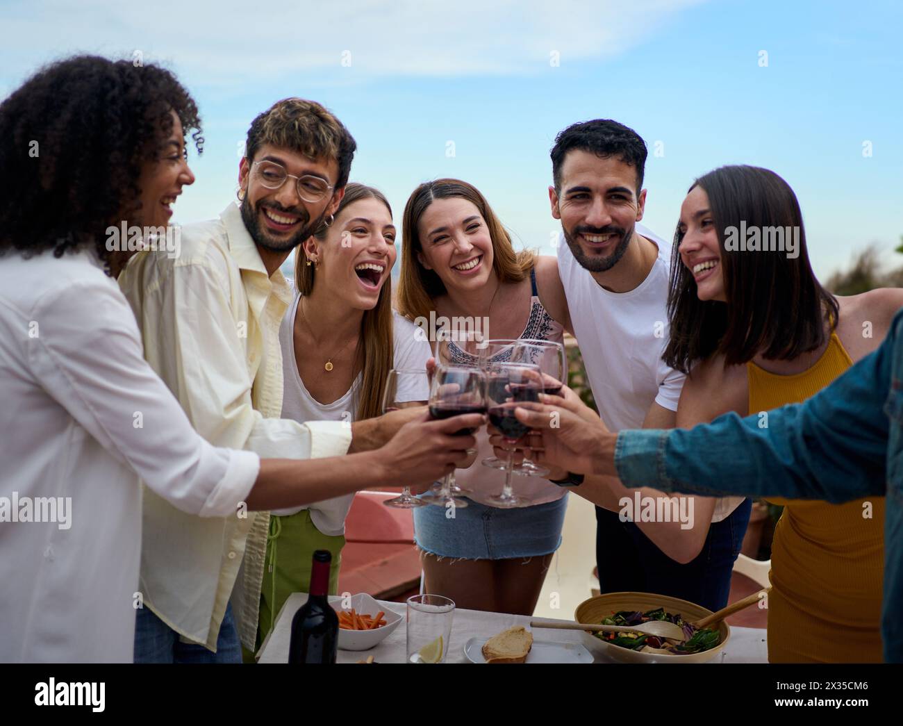 Incontro di giovani amici sorridenti che brindano a bicchieri di vino in piedi per celebrare un evento sulla terrazza Foto Stock