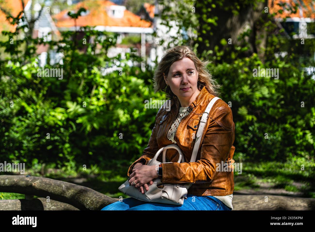 Bella donna bionda seduta su una panchina del parco che guarda lontano. Bella donna sposata in attesa di contemplazione, il suo sguardo si è voltato le spalle Foto Stock