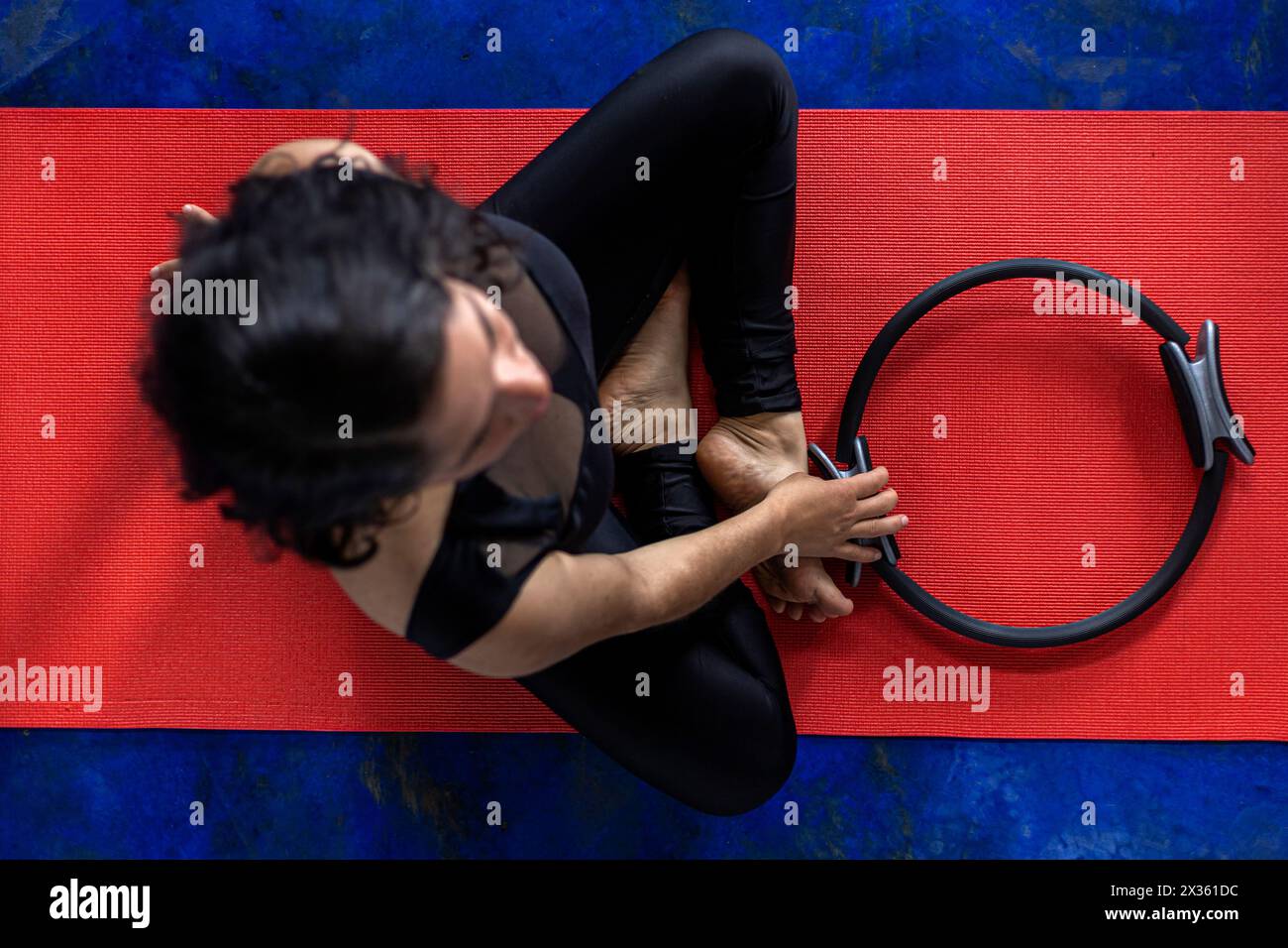 Vista dall'alto della donna latinoamericana (38) che fa esercizi tonificanti con l'anello di esercizio sul tappetino rosso per il fitness. Fondo blu. Studio yoga Foto Stock